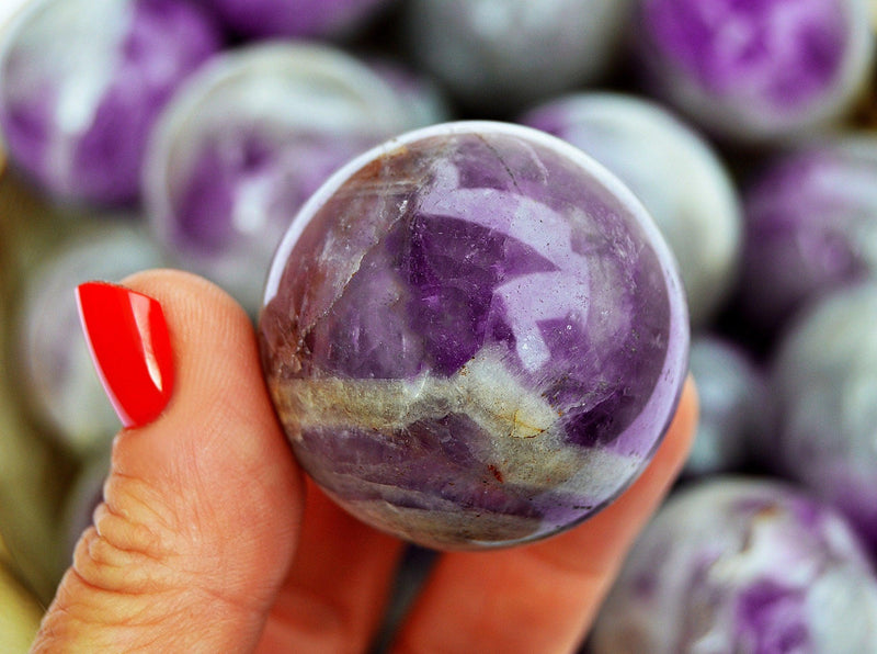One amethyst crystal sphere on hand with nackground with several crystals