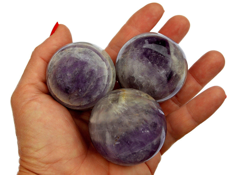 Three amethyst sphere stones 55mm - 60mm on hand with white background
