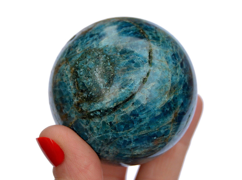 One blue apatite sphere crystal 55mm on hand with white background