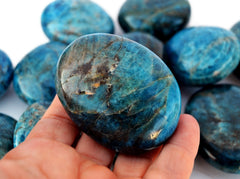 One large blue apatite palm stones 70mm on hand with background with several crystals