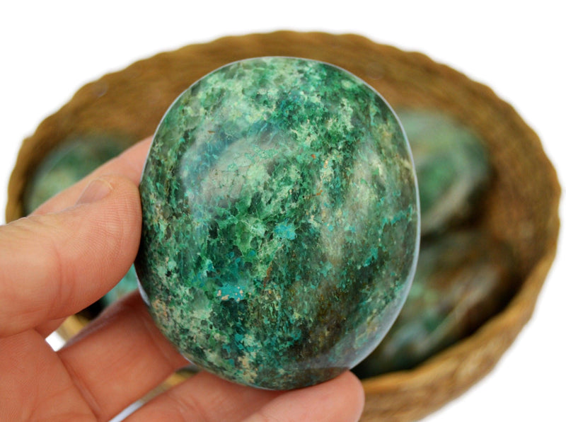 Large chrysocolla 70mm on hand with background with some crystals inside a basket
