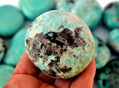 One green amazonite palm stone 60mm on hand with background with some crystals