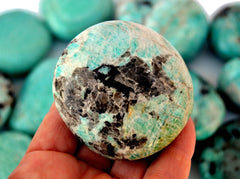 One green amazonite palm stone 50mm on hand with background with some crystals