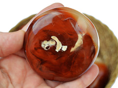 One red carnelian palm stone 70mm on hand with background with one stone inside a basket on white