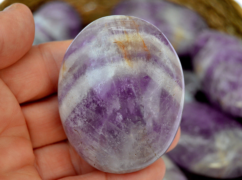 One amethyst crystal palm stone 60mm on hand with background with some crystals inside a basket