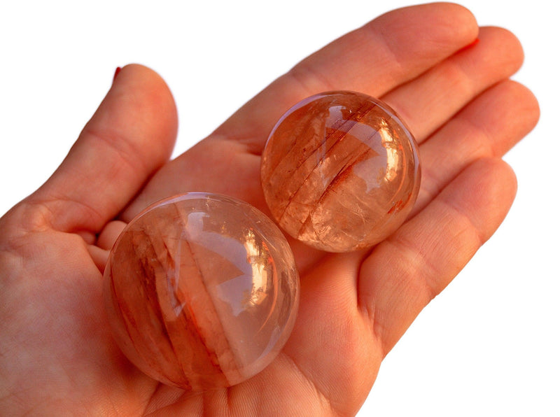 Two hematoid quartz crystal spheres 40mm - 30mm on hand  with white background