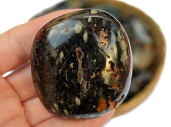 Large brown ocean jasper palm stone 60mm on hand with background with some stones inside a basket