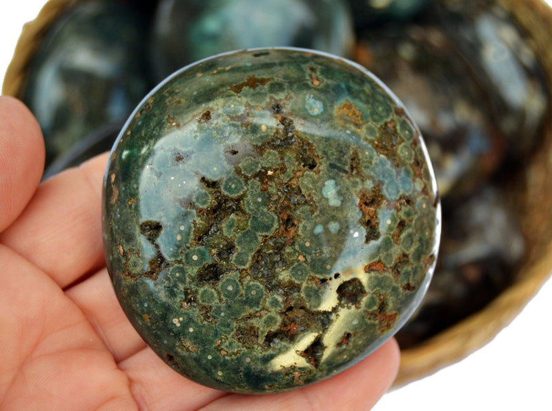 Big green ocean jasper palm stone 60mm on hand with background with some stones inside a basket