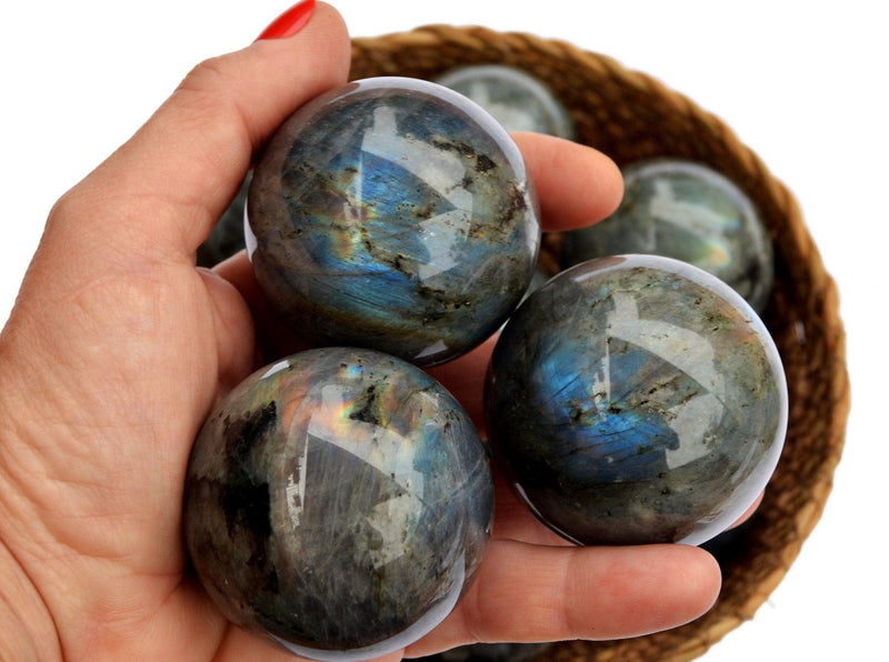 Three labradorite crystals spheres on hand with background with some balls inside a basket