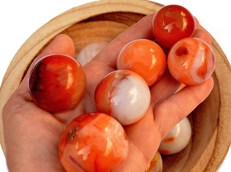 Several carnelian crystal spheres 35mm - 40mm on hand with background with some sphere stones inside a bowl