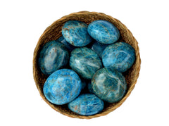 Several blue apatite palm stones inside a basket on white background