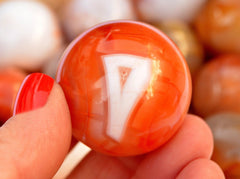 One carnelian crystal sphere 60mm on hand with background with some spheres