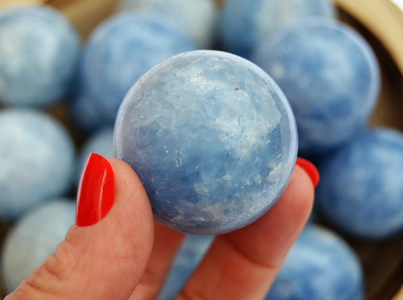 One blue calcite sphere 25mm on hand with background with some balls inside a wood bowl