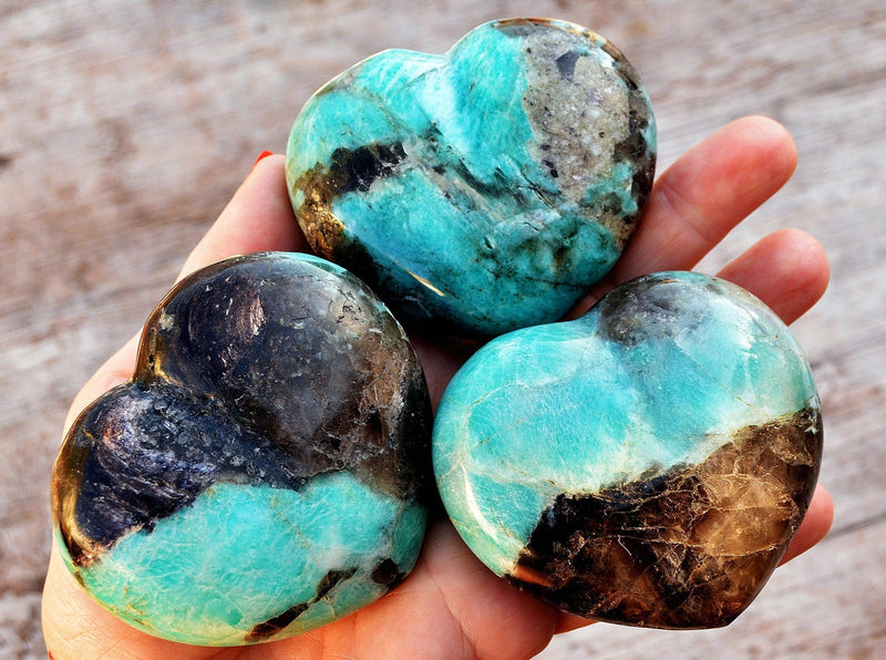 Three large amazonite heart stones 70mm on hand with wood background