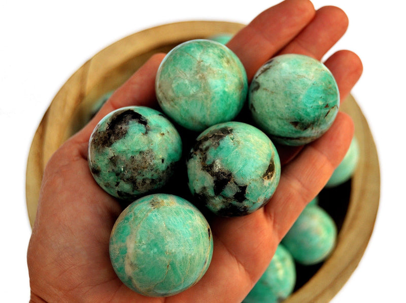 Some amazonite sphere stones 25mm-40mm on hand with background with some crystals inside a wood bowl