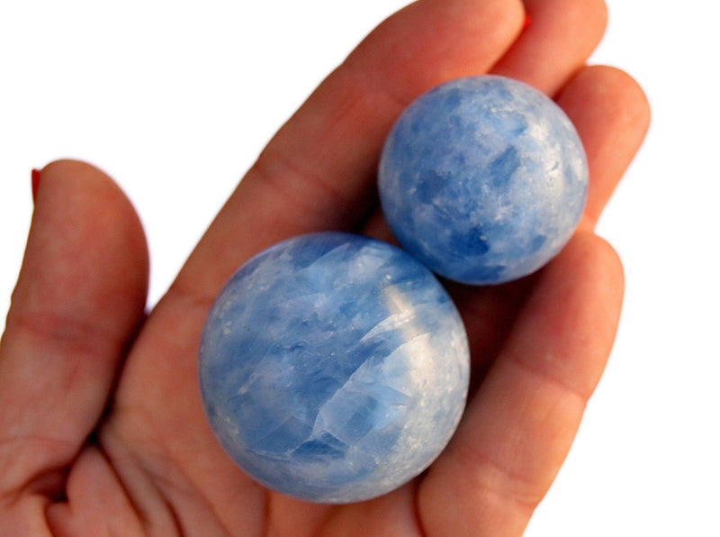 Two blue calcite crystal spheres 25mm-40mm on hand with white background