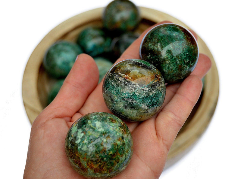 Three green chrysocolla sphere stones 40mm on hand with background with some balls inside a wood bowl