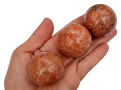Three orange calcite crystal spheres 25mm-30mm on hand with white background
