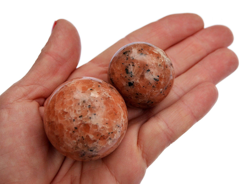Two orange calcite crystal spheres 25mm-40mm on hand with white background