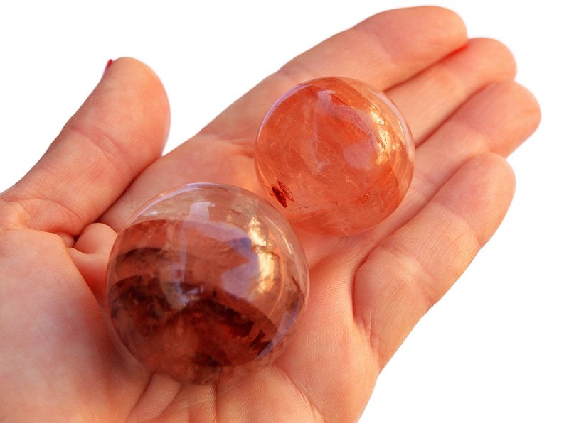 Two hematoid quartz crystal sphere stones 40mm - 25mm on hand with white background