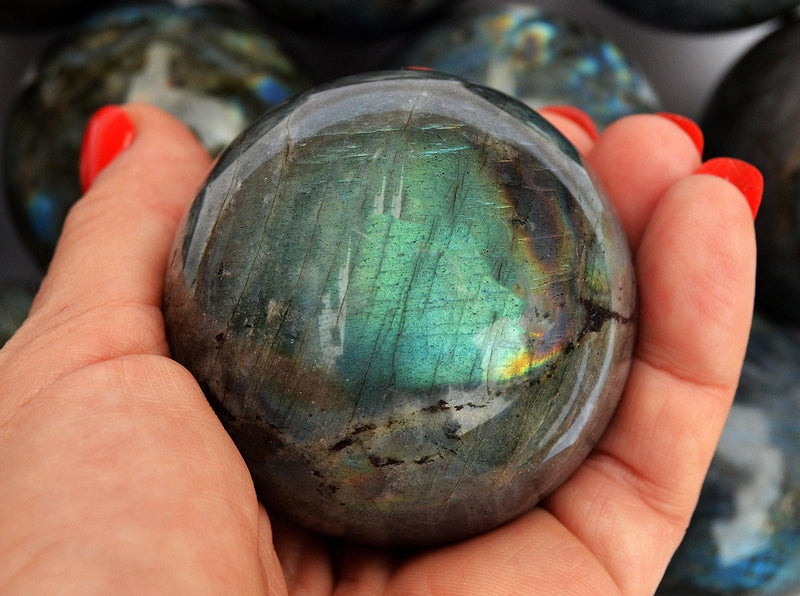 One green labradorite sphere 50mm on hand with white background