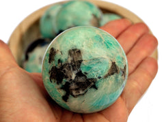 Amazonite crystal ball 45mm on hand with background with some stones inside a wood bowl