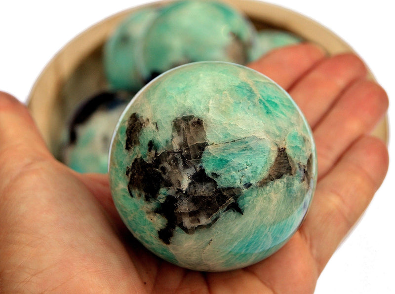 Green amazonite sphere 60mm on hand with background with some crystals inside a wood bowl