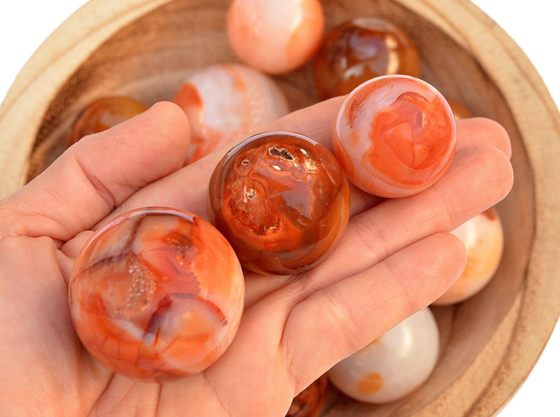 Three carnelian crystal balls 35mm - 40mm on hand with background with some spheres inside a bowl