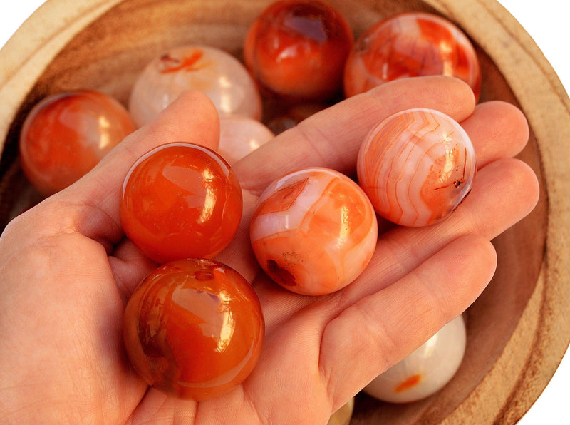 Three carnelian crystal spheres 30mm on hand with background with some sphere stones inside a bowl