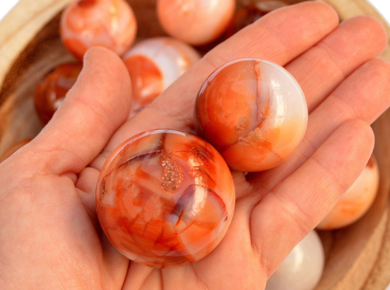 Two carnelian crystal spheres 40mm - 30mm on hand with background with some sphere stones inside a bowl