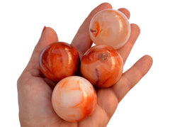 Four carnelian crystal spheres 45mm-50mm on hand with white background