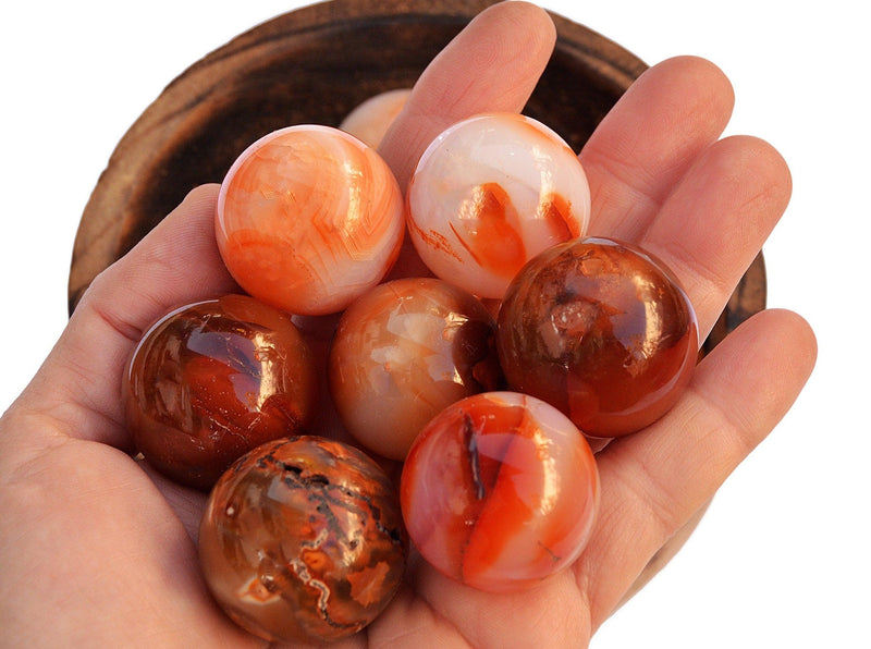 Seven carnelian spheres crystals 45mm-60mm on hand wiht background with wood bowl on white