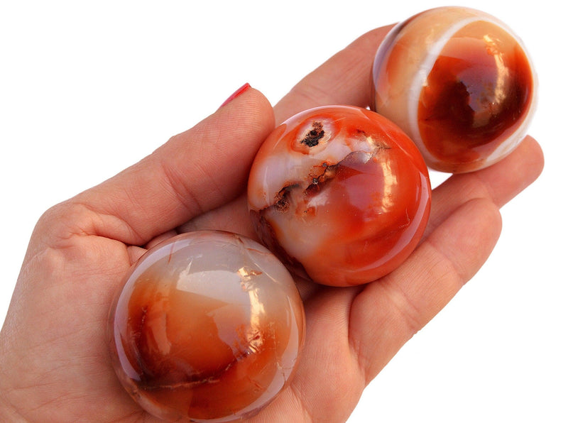 Three carnelian crystal spheres 50mm-60mm on hand with white background