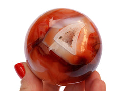 One druzy carnelian sphere stone 60mm on hand with white background