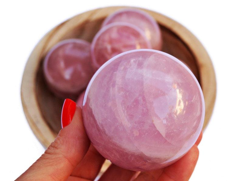 One large pink quartz sphere stone  on hand with background with some crystals inside a bowl