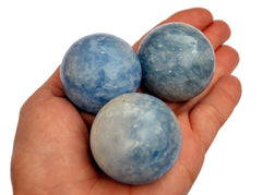 Three blue calcite sphere crystals 25mm-40mm on hand with white background