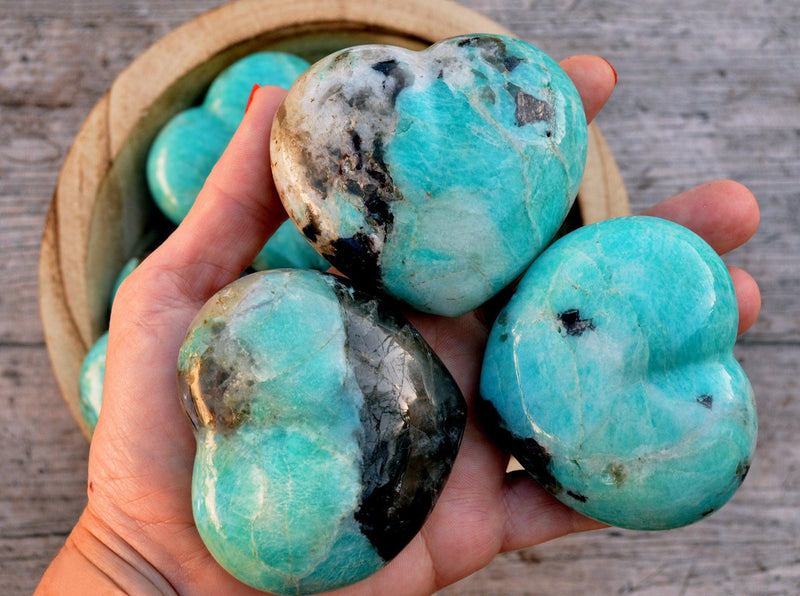 Three big amazonite puffy heart stones 70mm on hand with background with some crystals inside a bowl