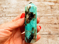 One amazonite crystal obelisk 95mm on hand with wood background