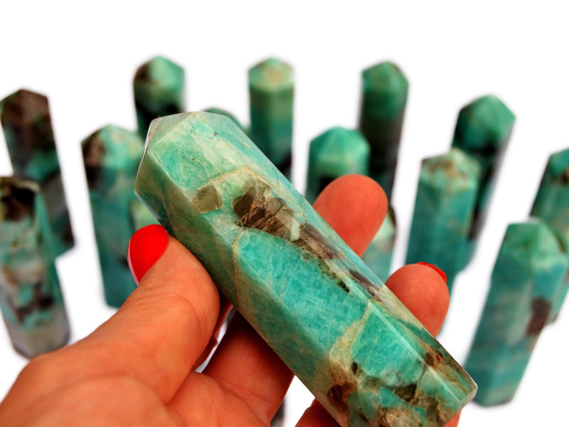 One amazonite crystal tower 95mm on hand with background with several stones