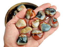 Ten  small polychrome jasper crystal hearts on hand with background with some crystals inside a wood bowl