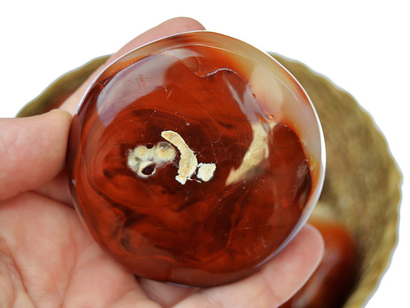 One red carnelian palm stone 70mm on hand with background with one stone inside a basket on white