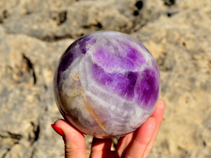 Big amethyst crystal sphere 80mm on hand with rock background