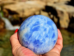 Large blue calcite sphere 85mm on hand with river landscape