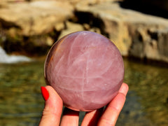 One large rose quartz sphere crystal 80mm on hand with background river landscape