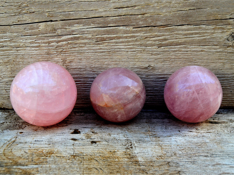 Three pink quartz crystal spheres 70mm-90mm on wood table