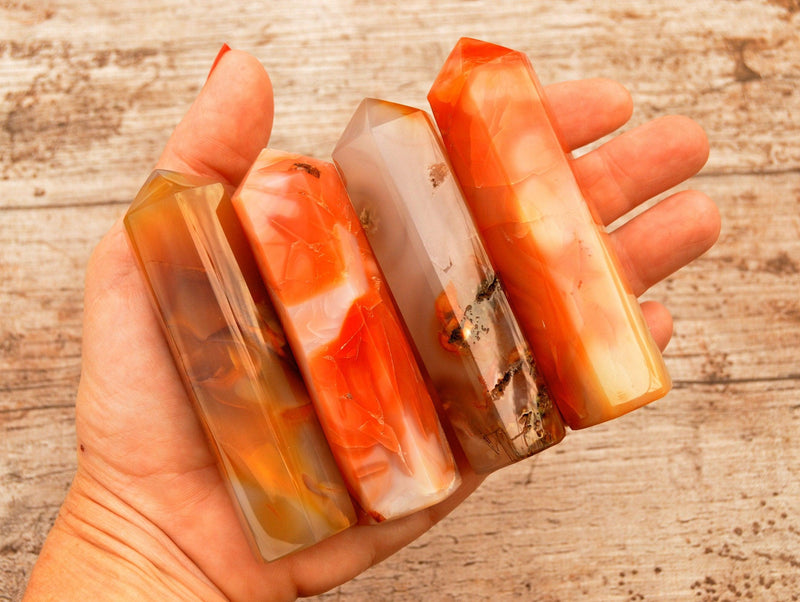 Four carnelian crystal towers 90mm on hand with wood backgroud