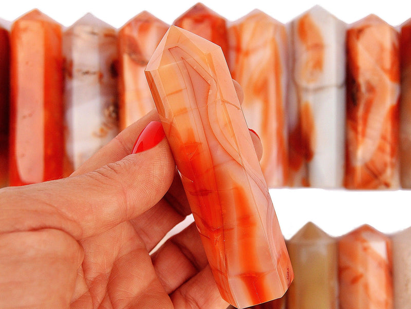 One carnelian faceted crystal point 90mm on hand with background with some obelisks on white