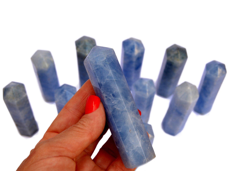 One blue calcite tower 90mm on hand with background with several obelisks on white