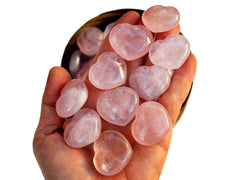 Some small pink quartz hearts 30mm on hand with background with some stones inside a bowl
