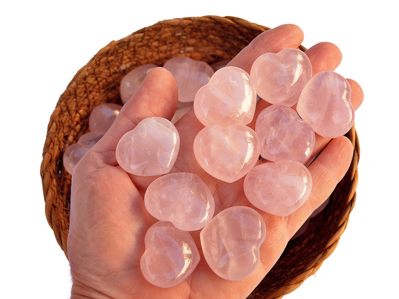 Ten rose quartz puffy heart crystals 30mm on hand with background with some crystals inside a straw basket on white